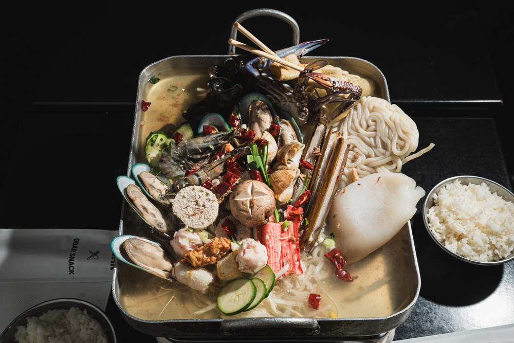 Diners cooking together at OBAR — tongs lifting from a sizzling tabletop grill